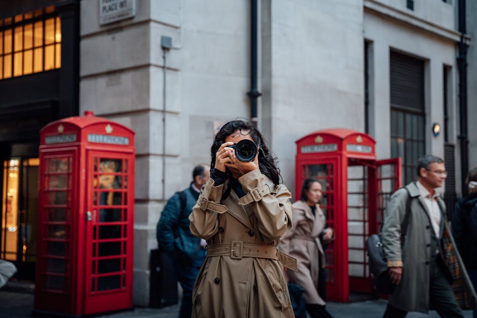 Woman photographing on a bustling London street with iconic red phone booths.